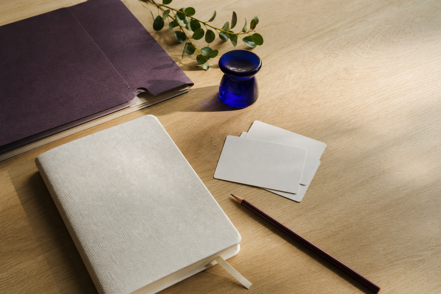 A desk with a notebook, planning cards and a blue glass vessel.